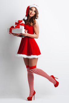 Full length portrait of beautiful girl in Santa Claus style dress and hat holding Christmas gifts