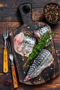 Cut smoked mackerel fish with herbs. Dark wooden background. Top view.