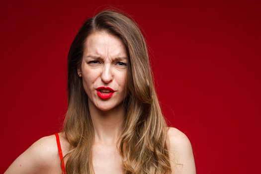 Head shot of young displeased serious female frowning on red studio background with copy space for advertising. High quality photo