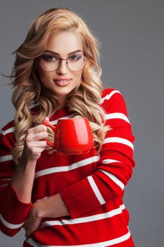 Beautiful woman in glasses and striped pullover holding red cup