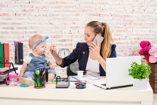 Family Business - telecommute Businesswoman and mother with kid is making a phone call. At the workplace, together with a small child