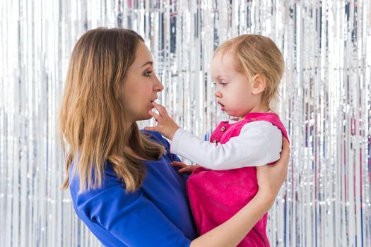 Childhood, holidays and family concept - Mother kissing baby daughter on shiny background. Close-up.