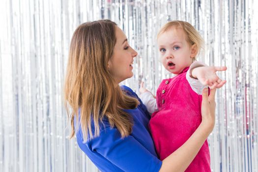 Childhood, holidays and family concept - Mother kissing baby daughter on shiny background. Close-up.