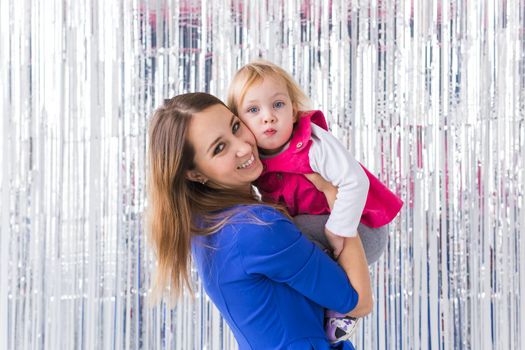 Childhood, holidays and family concept - Mother kissing baby daughter on shiny background. Close-up.