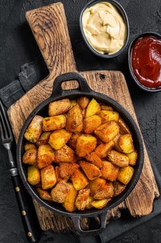 Patatas bravas, spicy potatoes, a Spanish dish with fried potato and a spicy garlic sauce. Black background. Top view.