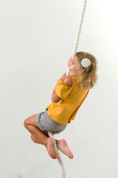 Cheerful little girl holding a rope with her hands. She tries to swing from side to side on it. Sport, fitness concept. Isolated over white background.