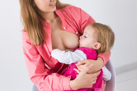 Lactation and motherhood concept - Young beautiful mother holding breastfeeding baby sitting on chair