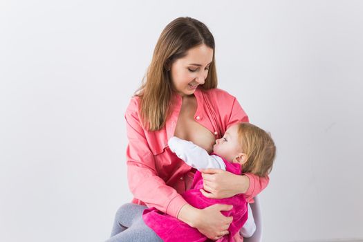 Lactation and motherhood concept - Young beautiful mother holding breastfeeding baby sitting on chair