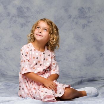 Beautiful little girl is sitting on the floor in the studio. The concept of a happy childhood, beauty and fashion.