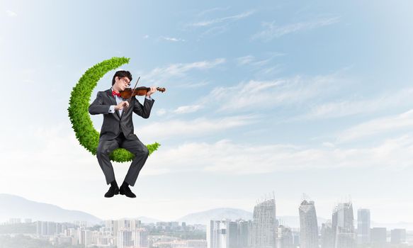 young businessman with a violin. sits on the moon symbol of plants. concept of inspiration in business