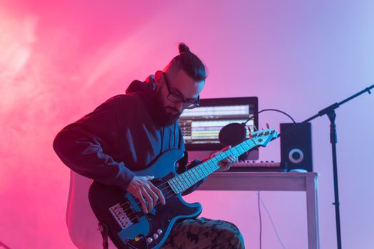 Create music and a recording studio concept - Bearded man guitarist recording electric guitar track in home studio.