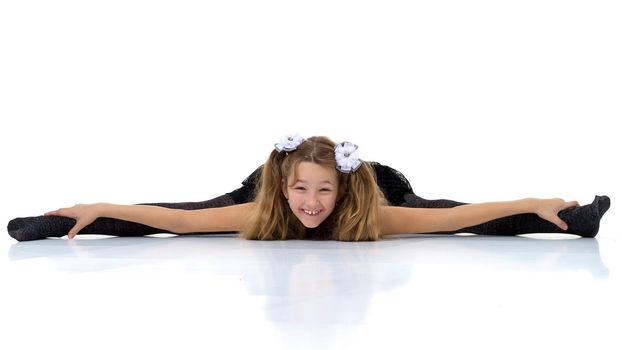 Girl sitting on floor with her legs wide apart. Pretty blonde girl pigtails in fashionable clothes posing in studio against white background. Preteen child wearing in black lace skirt and tank top