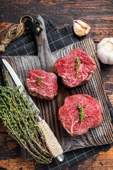 Prime raw Fillet mignon steaks on a wooden board with thyme and garlic. Dark wooden background. Top view.