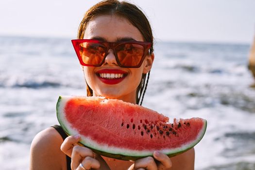 cheerful woman in sunglasses eating watermelon by the ocean. High quality photo