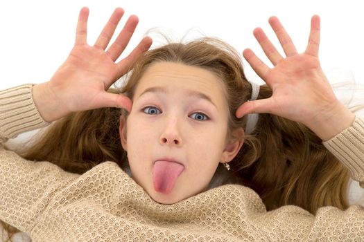 Happy preteen girl showing tongue and gesturing. Funny blonde girl wearing knitted jumper making funny face looking at camera against white background.