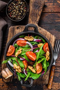 Healthy bistro green salad with mix leaves mangold, swiss chard, spinach, arugula and nuts in a pan. Dark wooden background. Top view.