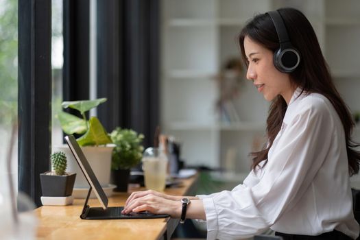 Side view head shot smiling asian woman freelancer wearing headset, communicating with client via video computer call. Millennial pleasant professional female tutor giving online language class.