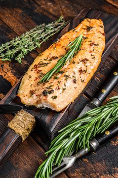 Baked trout fillet on a cutting board. Dark wooden background. Top view.