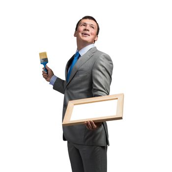 Creative businessman painter holding paint brush and whiteboard in hands. Portrait of handsome young man in business suit and tie isolated on white background. Inspiration and creativity in business.