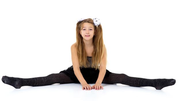 Girl sitting on floor with her legs wide apart. Pretty blonde girl pigtails in fashionable clothes posing in studio against white background. Preteen child wearing in black lace skirt and tank top
