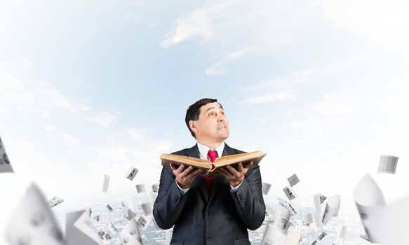 Happy businessman looking up with open book. Smiling man in suit standing on downtown background with falling paper documents. Lawyer holding legal regulation book. Business accounting and consulting
