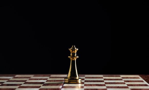 Golden queen chess figure standing on chessboard. Intellectual and tactic game. Strategy planning, leadership and teamwork business concept. Close-up one gold chess piece on black background.