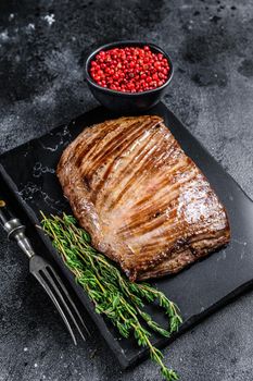 Grilled flank beef meat steak on a marble board. Black background. Top view.