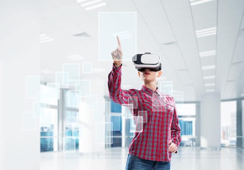 Woman in casual wearing virtual reality mask and touching icon on screen. Mixed media