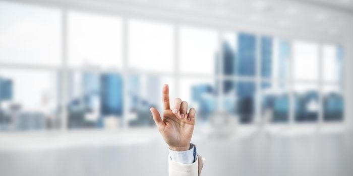 Close of businesswoman hand touching screen with finger and office at background