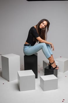 beautiufl caucasian woman with charming appearance sits on a white cube and looks to te camera, picture isolated on white background