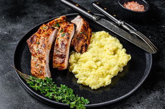 Sliced BBQ grilled pork rack spare ribs on a plate with mash potato. Black background. Top view.