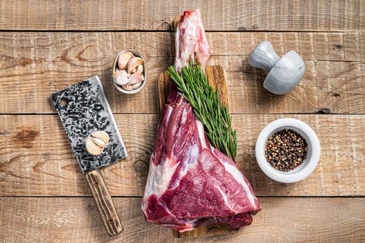 Raw lamb mutton leg with rosemary and pepper on cutting board. wooden background. Top view. Copy space.