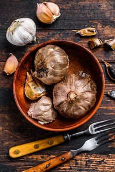 Bulbs and cloves of fermented black garlic in a plate. Dark wooden background. Top view.