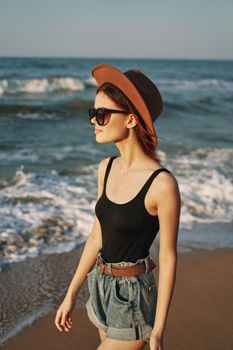 cheerful woman in sunglasses and a hat walks along the ocean. High quality photo