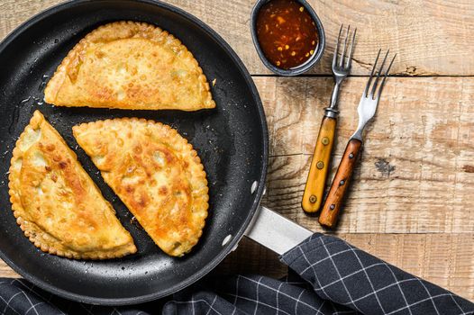 Homemade fried chebureks with meat and herbs in a pan, traditional Caucasian cuisine. Wooden background. Top view. Copy space.