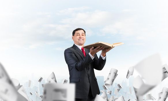 Happy businessman holding old open book. Smiling man in suit standing on downtown background with falling paper documents. Lawyer holding legal regulation book. Business accounting and consulting
