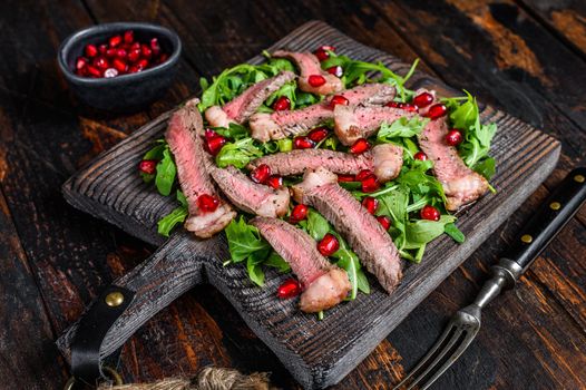 Grilled Beef Steak salad with arugula, pomegranate and greens vegetables. Dark wooden background. Top view.