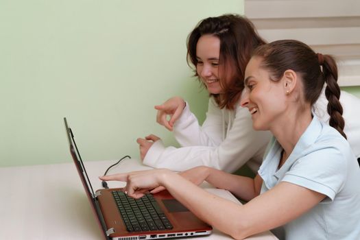 Spike conversation. Portrait of two pretty young women sitting at home and having a internet conversation on a laptop. The concept of stay at home, quarantine