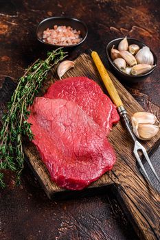 Raw rump beef meat steaks on butcher wooden board. Dark background. Top view.