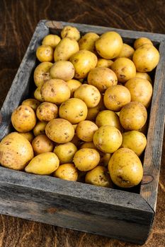 Young baby Potatoes in a wooden box. Wooden background. Top view.