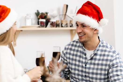 Young couple in Santa hats drinking wine and celebrating Christmas, close up