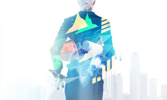 Woman architect standing with technical blueprints and safety helmet. Back view of engineer on background of cityscape. Double exposure with financial diagrams. Engineering and development company.