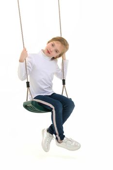 Beautiful little girl swinging in the studio on a swing. Concept of a happy childhood, family well-being.