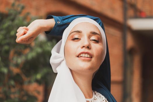 Portrait of young muslim woman wearing hijab head scarf in city while looking at camera. Closeup face of cheerful woman covered with headscarf smiling outdoor. Islamic girl outdoors