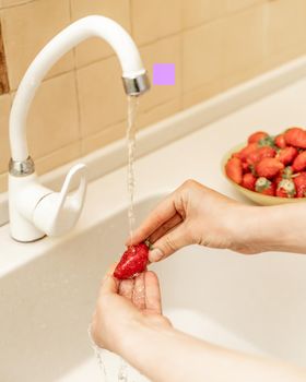 Women's hands wash strawberries and blueberries under a stream of water in the kitchen sink. Selective focus. Wash fruit before eating.