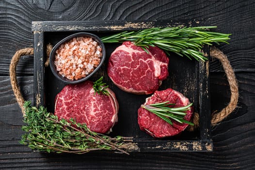 Fillet Mignon tenderloin raw meat veak steaks in wooden tray with herbs. Black wooden background. Top view.