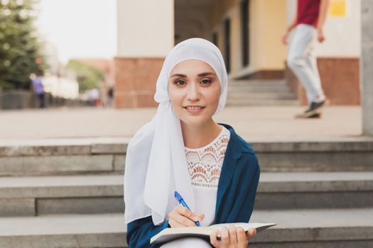 Female middle eastern college student sits on stairs in university campus. Education concept
