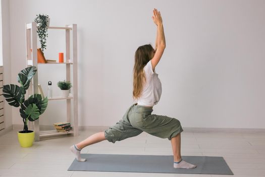 Woman practise yoga performs. Pose on mat inside of cozy room with plants and greenery. Healthy lifestyle