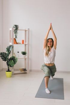 Woman practise yoga performs. Pose on mat inside of cozy room with plants and greenery. Healthy lifestyle