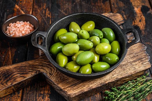 Green big olives in bowl with thyme. Dark wooden background. Top view.